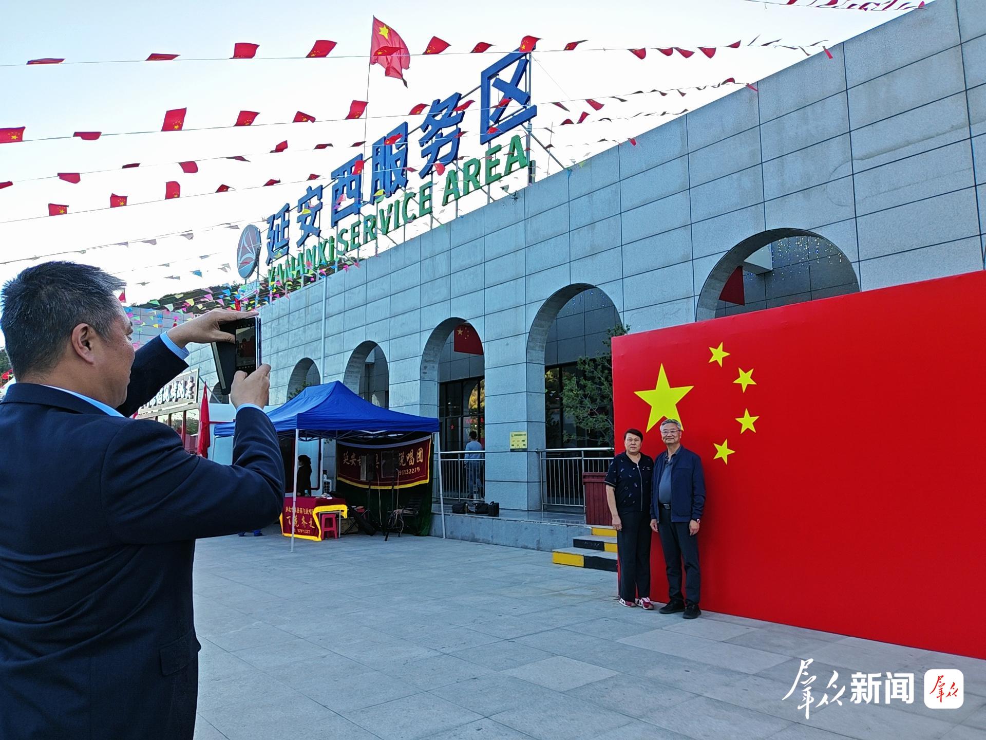 10月1日,在包茂高速延安西服务区,工作人员帮路过的司乘人员在设置的国旗背景墙前拍照留念。 群众新闻记者 霍海澎摄